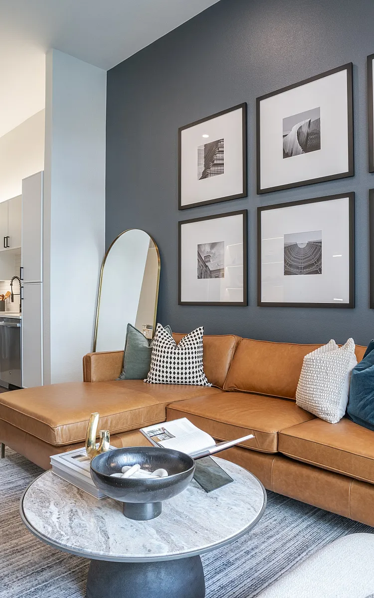 Modern apartment living room featuring a stylish leather sectional, contemporary art wall, and elegant kitchen with a breakfast bar.