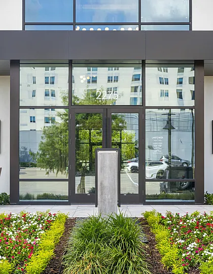Modern apartment entrance adorned with vertical green wall and vibrant flowerbeds, featuring sleek glass doors and contemporary design elements.
