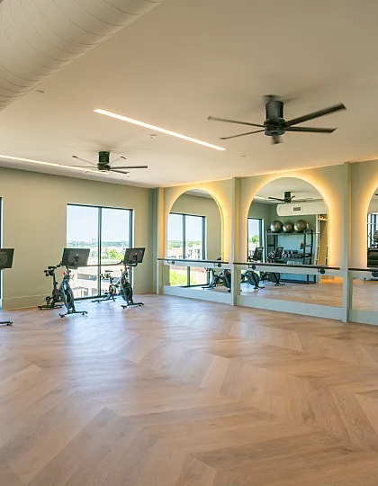 Modern fitness studio with sleek wooden flooring, exercise bikes, and full-length mirrors reflecting natural light.