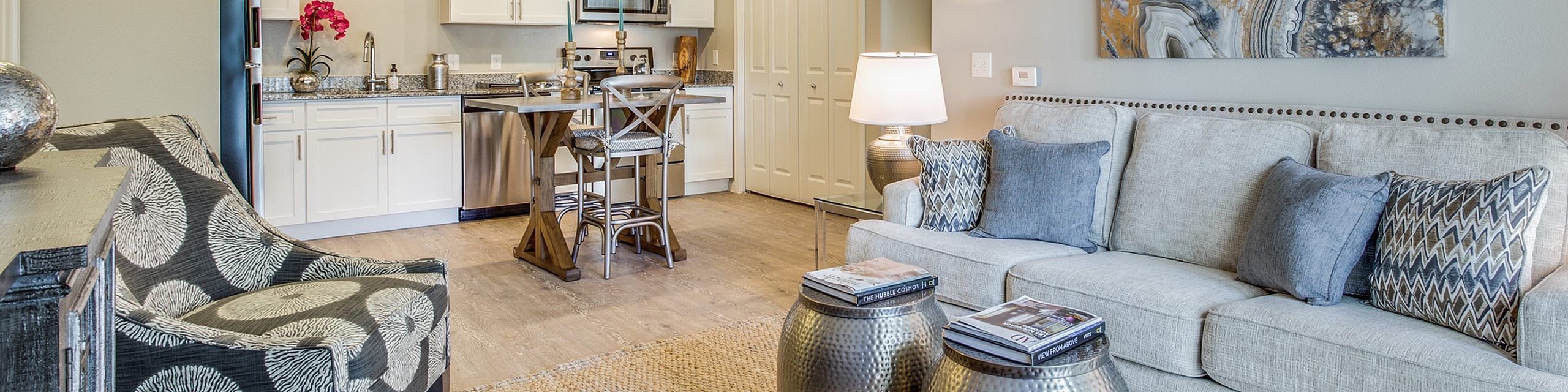 Chic open-concept living room featuring a stylish sofa, modern kitchen with white cabinetry, and elegant decor in a cozy setting.