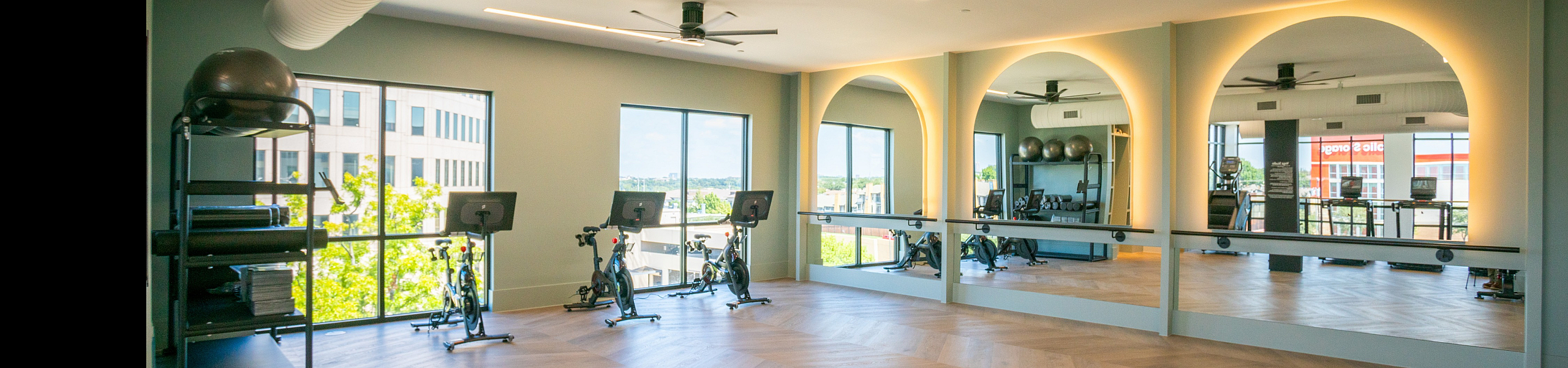 Modern fitness room featuring floor-to-ceiling mirrors, sleek wooden flooring, and cycling equipment set against large windows with a scenic view.