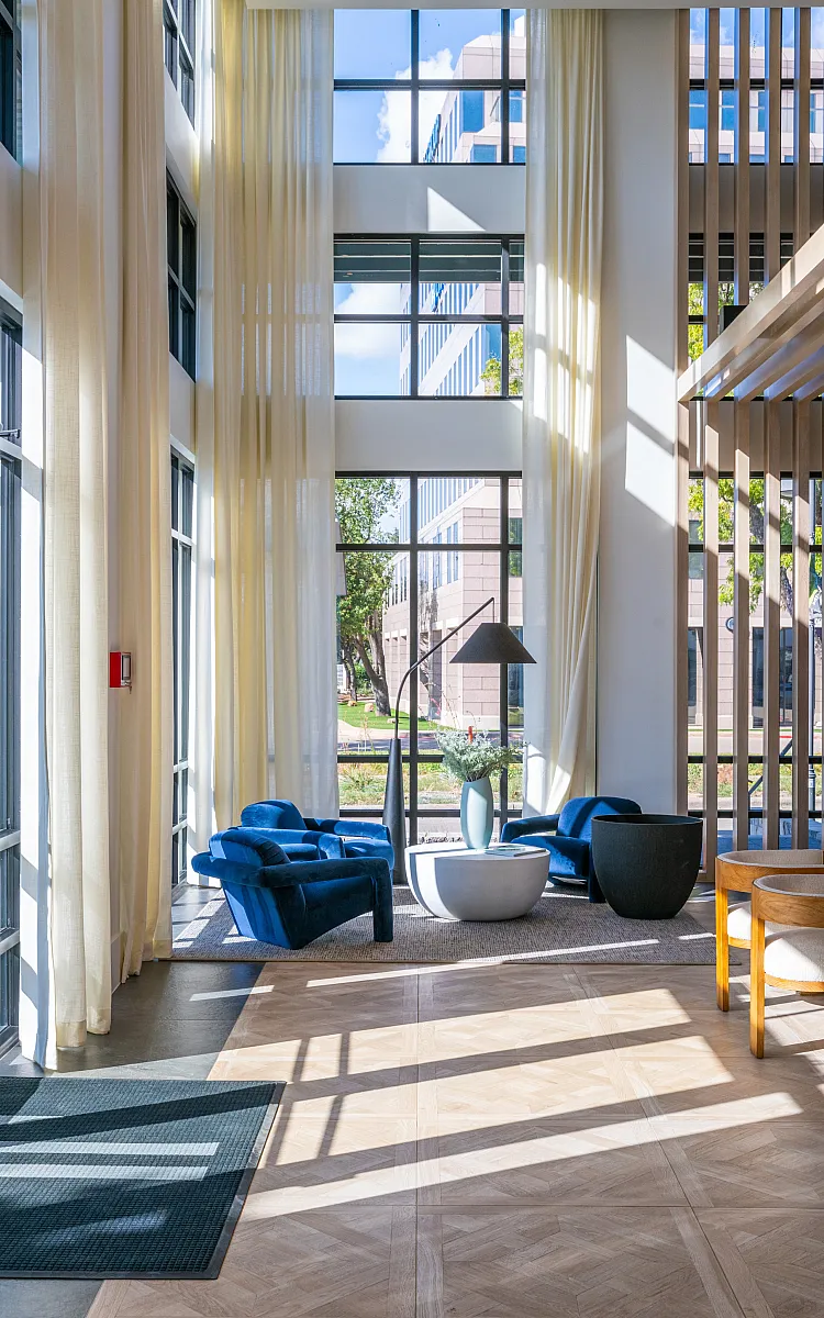 Bright and airy modern lounge area with high ceilings, large windows, and stylish blue armchairs inviting natural sunlight.