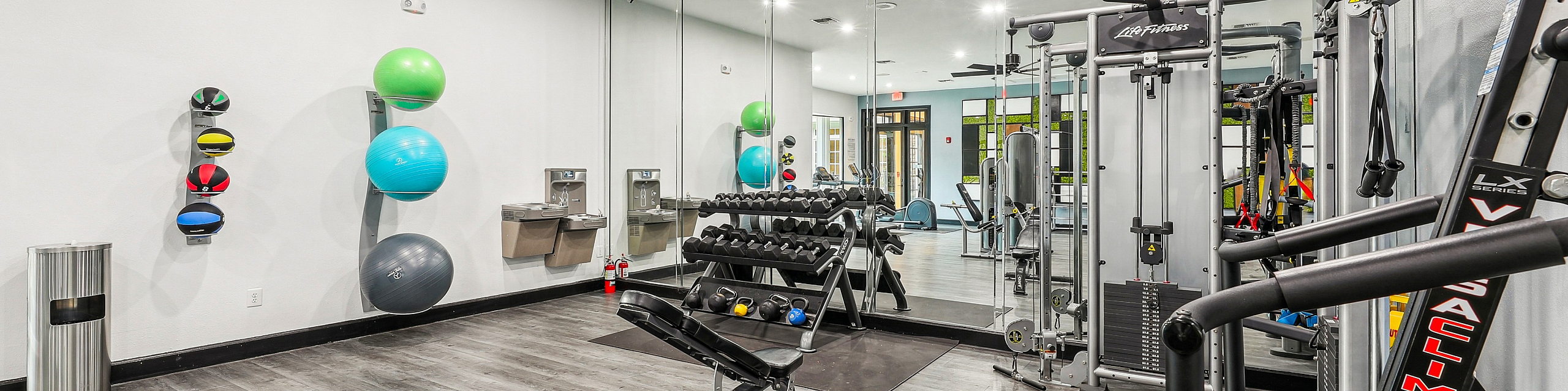 Modern apartment gym with sleek exercise equipment, mirrored walls, and a stylish wooden floor offering a vibrant workout space.