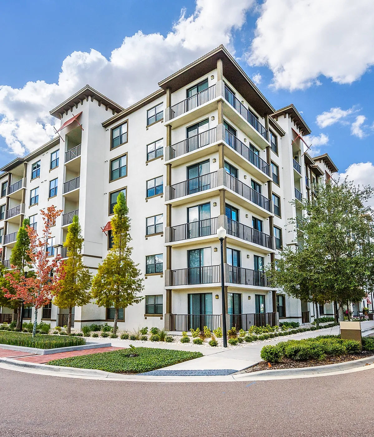 Modern apartment building with elegant balconies, surrounded by lush landscaping and vibrant autumn trees under a clear blue sky.