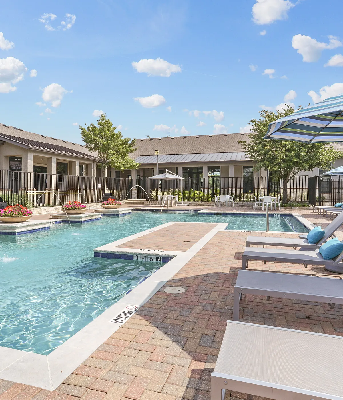 Luxurious apartment community pool with elegant lounge chairs, vibrant flower accents, and shade-providing umbrellas, perfect for relaxation and leisure.