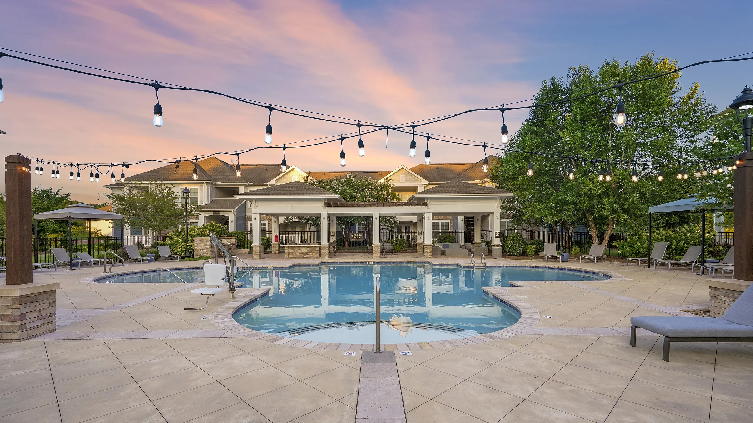 Luxurious poolside retreat at sunset with elegant lighting, comfortable lounge chairs, and lush greenery, offering a serene outdoor escape.