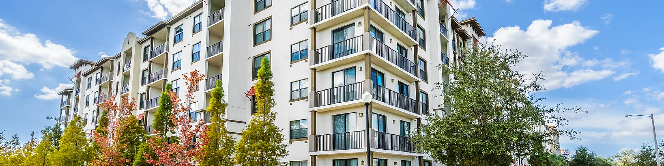 Modern apartment building with striking architectural design, featuring multiple balconies and beautiful landscaping under a clear blue sky.