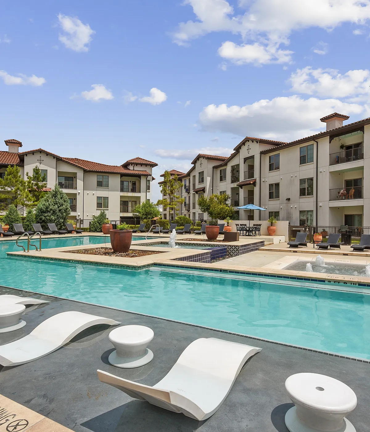 Luxurious apartment complex with a stunning swimming pool, modern lounge chairs, and elegant architecture set against a vibrant sky.