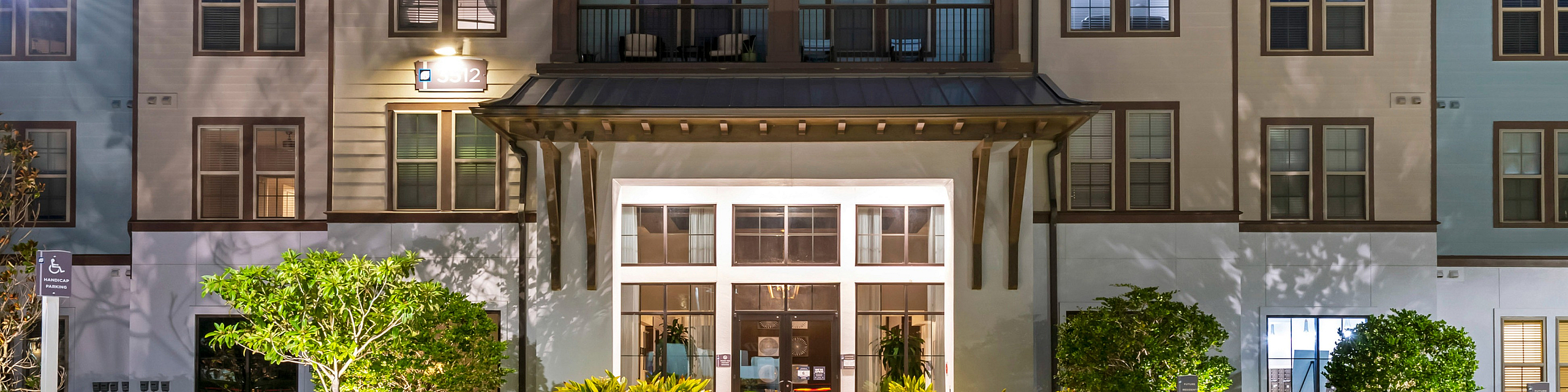 Elegant three-story apartment building with beautiful landscaping and a welcoming entrance under a twilight sky.