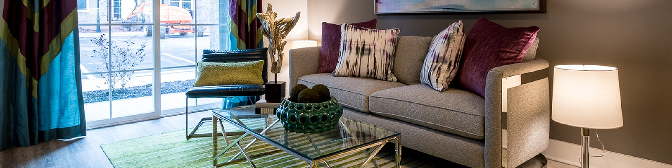 Chic living room with modern sofa, vibrant decor, and natural light from large windows.