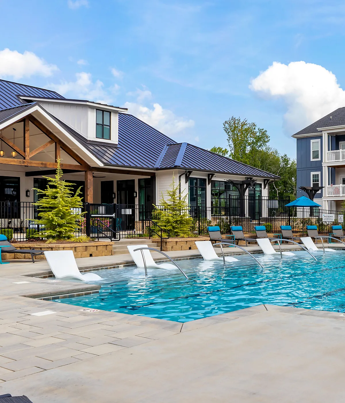 Luxurious apartment complex with resort-style pool, modern lounge chairs, and blue umbrella-covered seating areas.