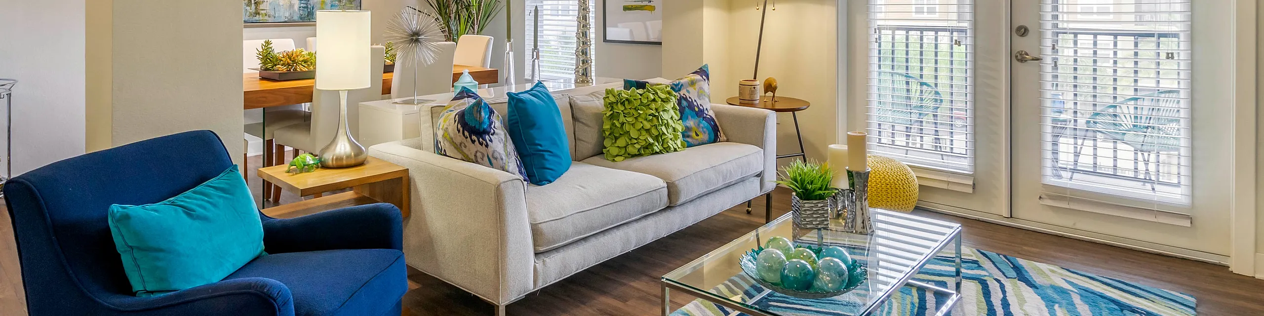 Chic and modern living room with vibrant decor, featuring a cozy sofa, elegant armchair, stylish glass coffee table, and large windows with abundant natural light.