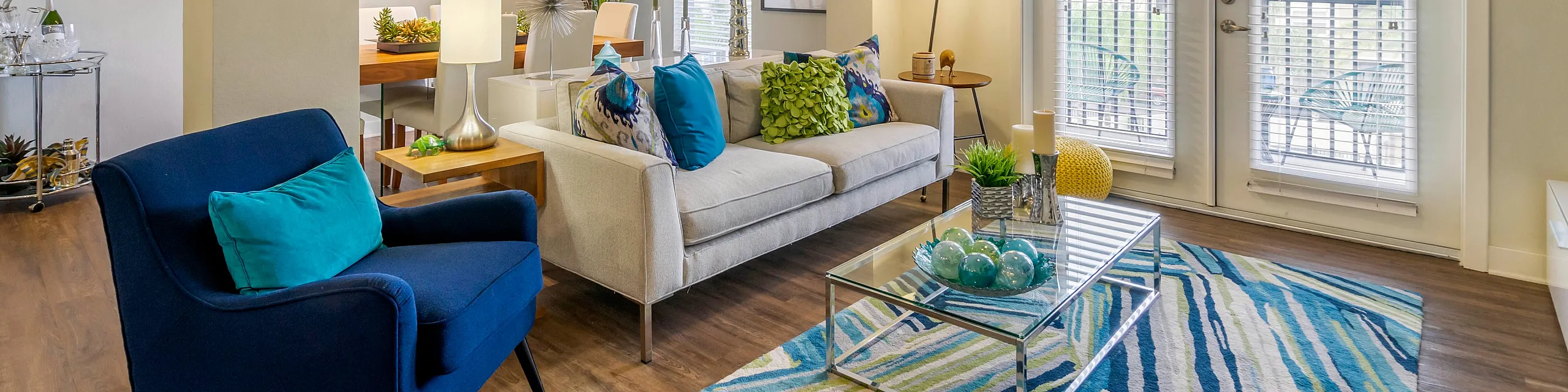 Bright and modern living area with vibrant decor, featuring a cozy sofa and stylish armchair, accentuated by a colorful rug and elegant lighting.