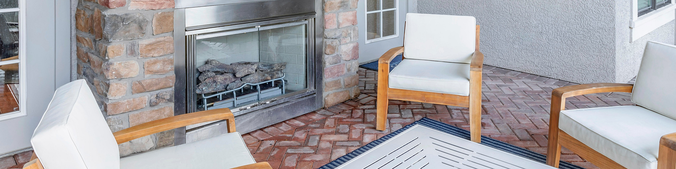 Inviting outdoor patio with cozy modern seating around a stylish stone fireplace, featuring artistic wall decor and elegant brick flooring.