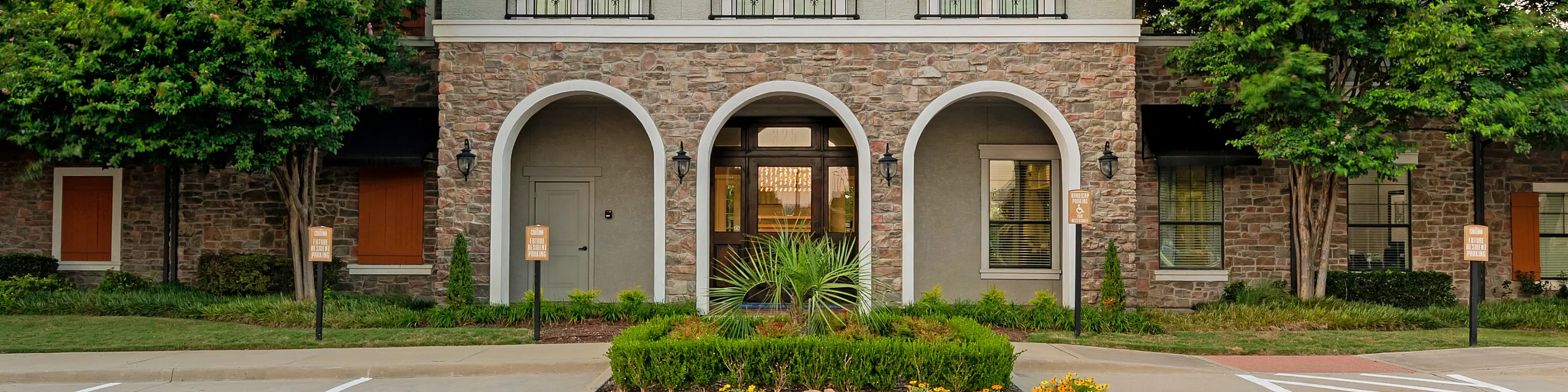 Charming residential building with stone facade, elegant arches, and lush landscaping under a serene sky.