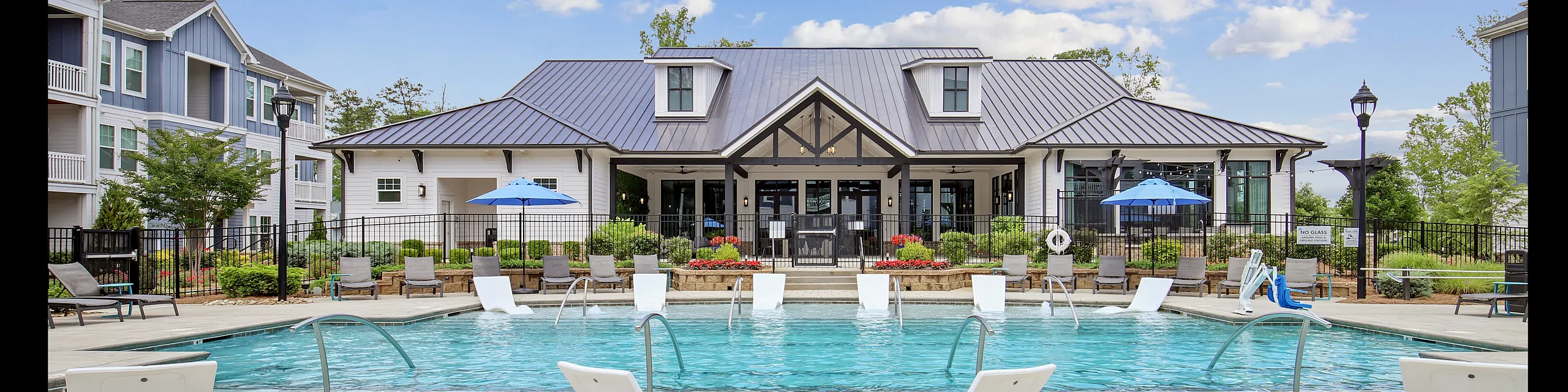 Luxurious apartment community featuring a sparkling outdoor pool, modern clubhouse, and elegant lounge chairs, set under a clear blue sky.