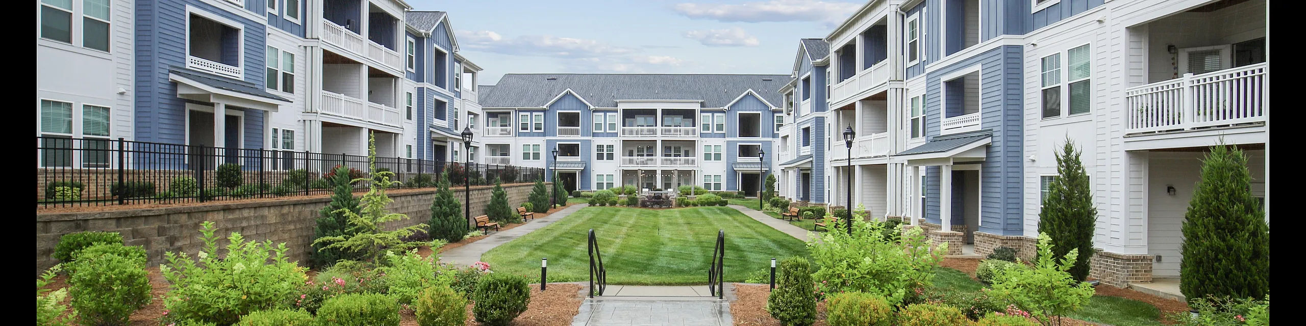 Charming apartment complex with modern blue and white architecture, lush landscaped gardens, and a welcoming courtyard.