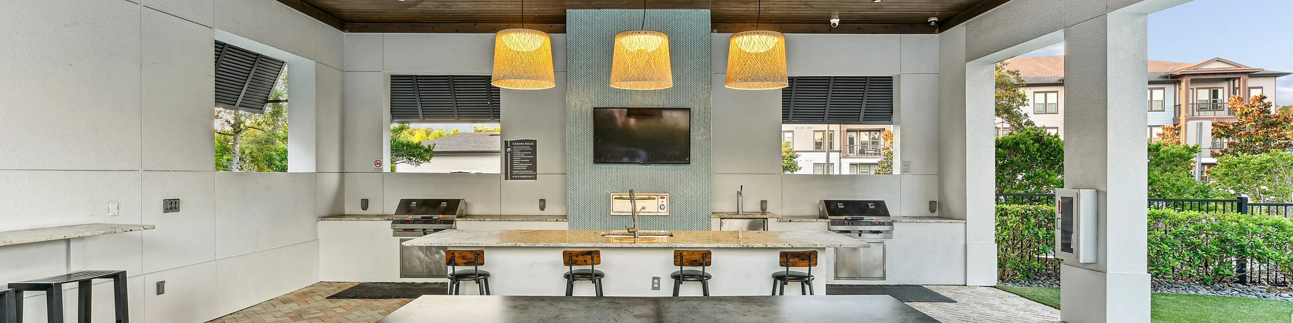 Chic outdoor entertainment space featuring a ping pong table, modern built-in grills, elegant bar seating, and ambient lighting under a wooden ceiling.