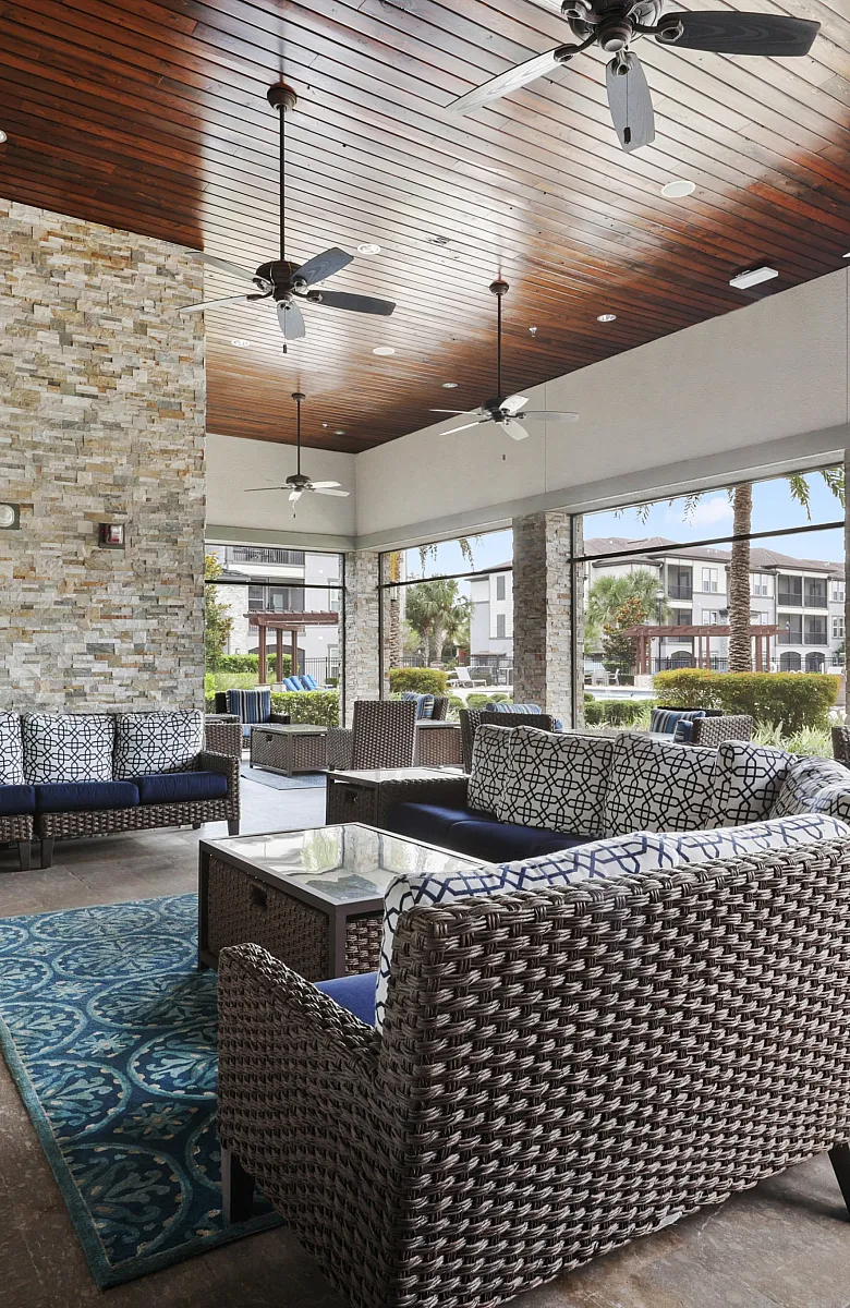 Luxurious outdoor lounge area with stylish wicker seating, cozy patterned cushions, stone fireplace, and spacious views of a modern apartment complex.