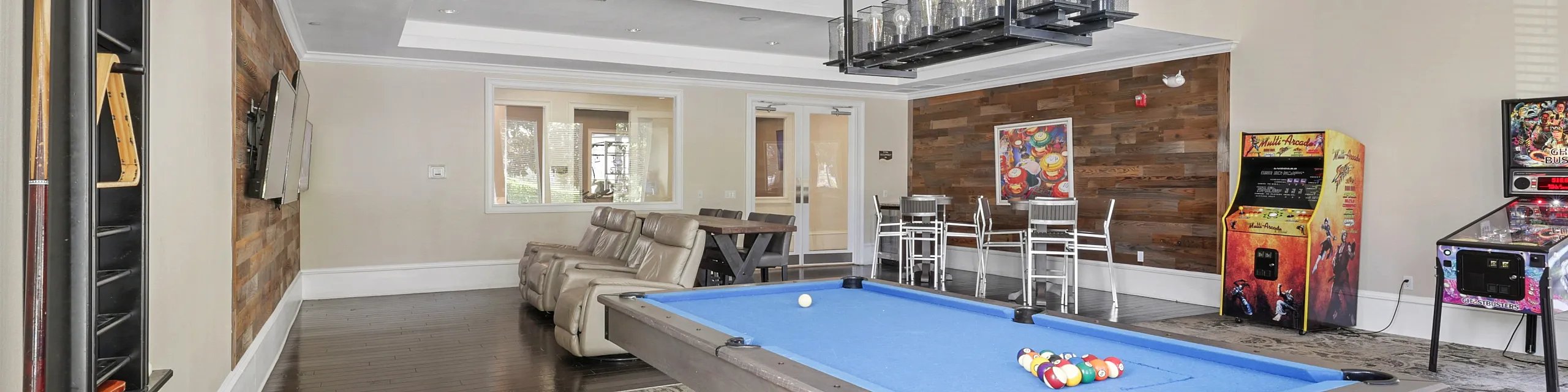 Luxurious game room featuring a sleek blue pool table, arcade machines, stylish seating, and modern lighting, perfect for entertaining.