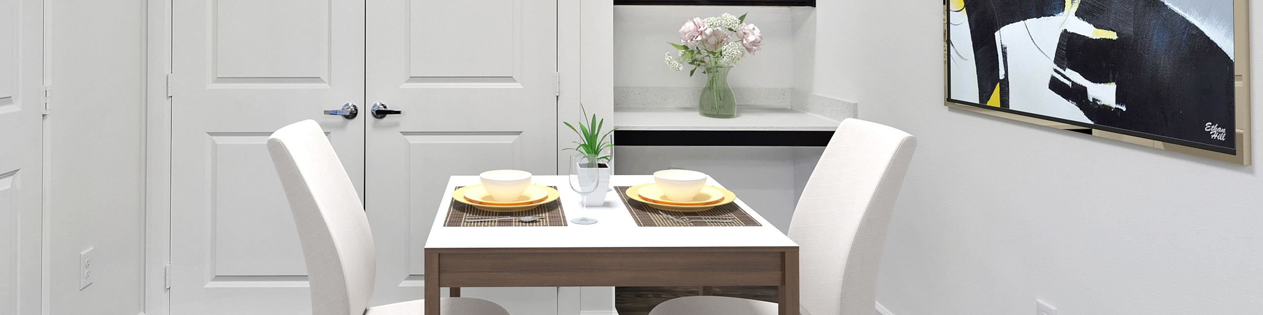 Chic dining nook with modern white chairs and a wooden table set for two, highlighted by abstract wall art and elegant cabinetry.