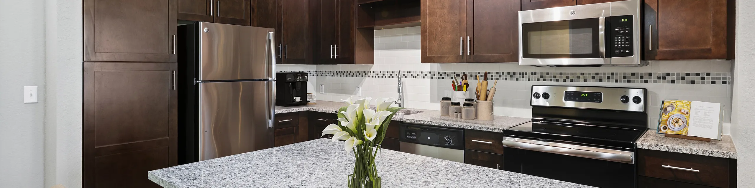 Modern kitchen with granite countertops, stainless steel appliances, and elegant dark wood cabinetry, enhanced by ambient lighting.