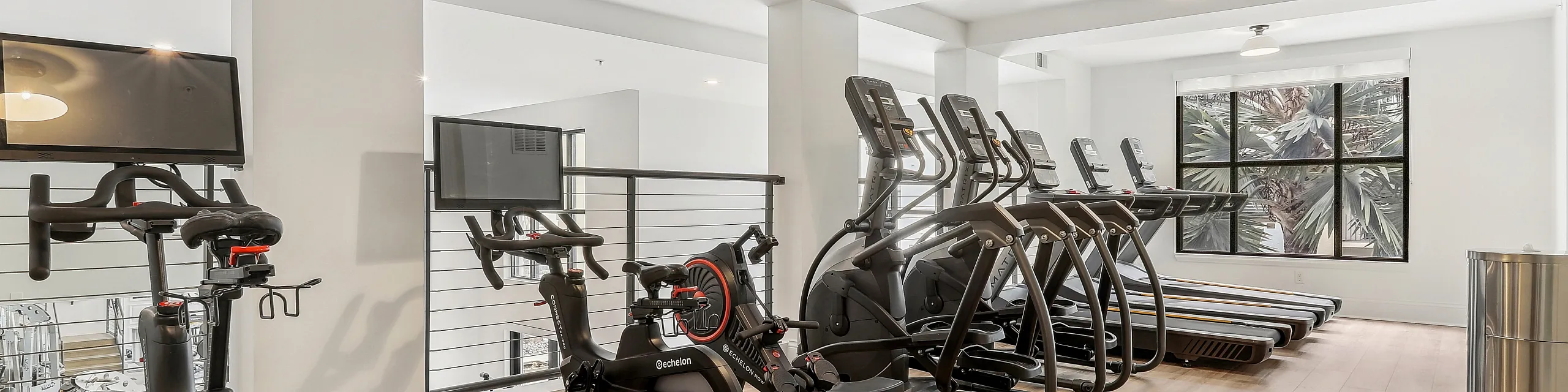 Bright, modern fitness center with sleek exercise bikes and treadmills, set against large windows offering scenic views.