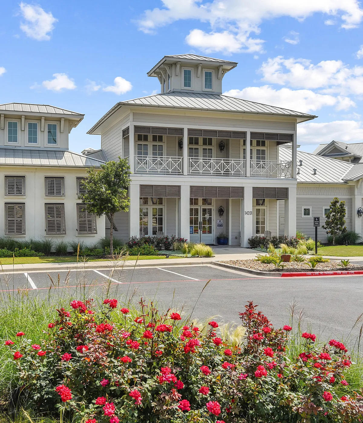Charming, elegant building with modern architecture, surrounded by lush gardens and vibrant flowers, under a bright blue sky.