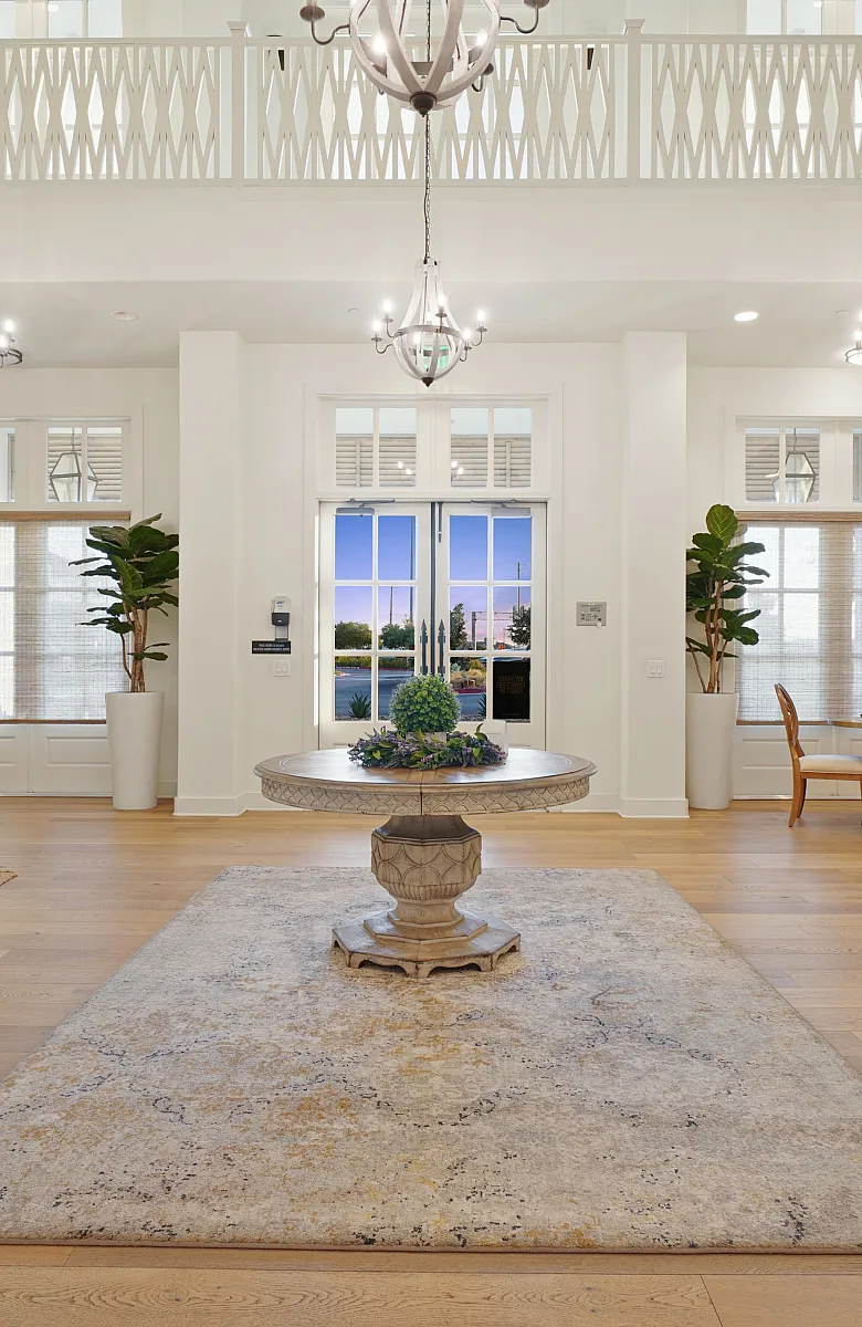 Elegant and spacious living area with high ceilings, stylish chandeliers, and natural light. Features cozy seating, lush greenery, and artistic decor for a welcoming atmosphere.