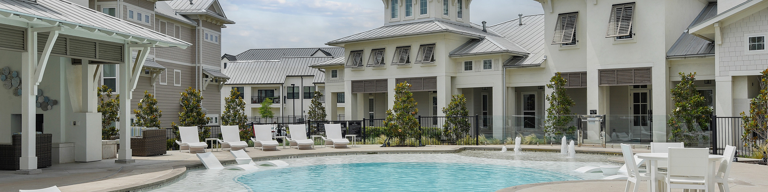 Luxurious apartment complex with a sparkling outdoor pool, stylish sun loungers, and modern architecture under a bright blue sky.
