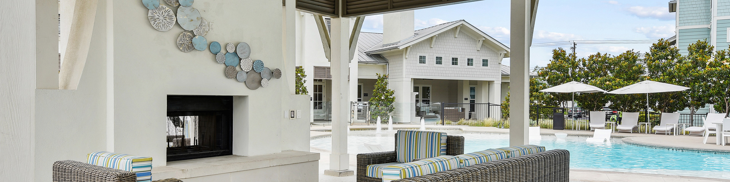 Elegant outdoor seating area with wicker furniture and vibrant cushions, overlooking a serene pool, under a charming pavilion with artistic wall decor.