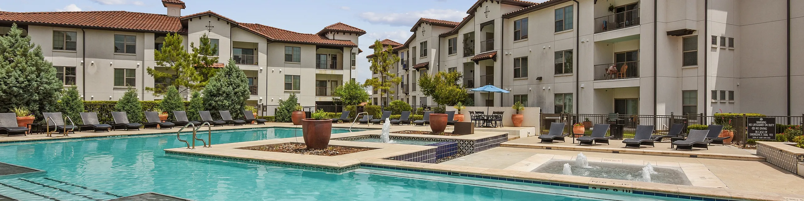 Luxurious apartment complex featuring a sparkling outdoor pool with relaxing lounge chairs and vibrant landscaping against a backdrop of modern architecture.