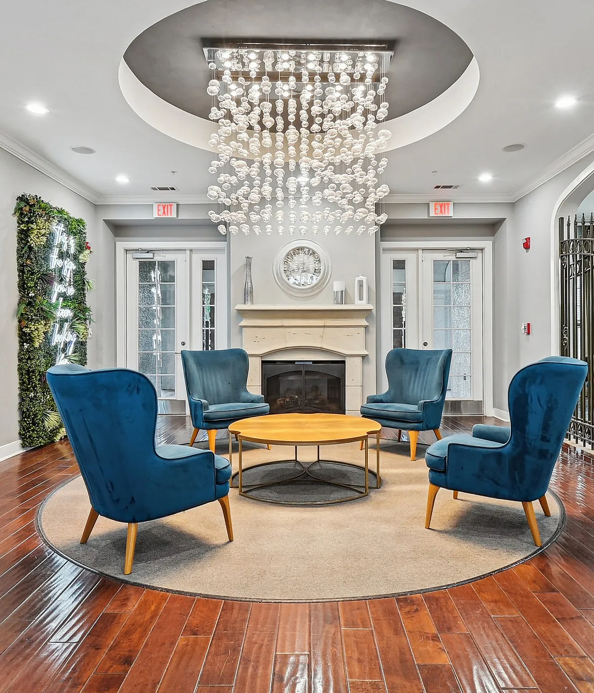 Elegant apartment lobby featuring a modern chandelier, plush blue armchairs, and a cozy fireplace, perfect for welcoming guests.