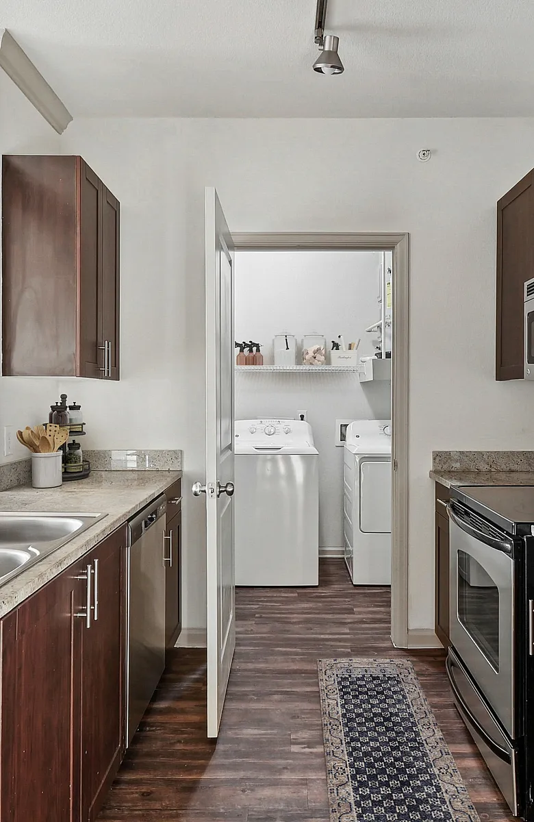 Modern kitchen with sleek stainless-steel appliances, rich wooden cabinetry, and a view into a convenient laundry area.