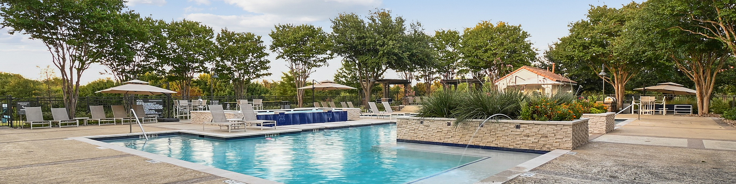 Inviting outdoor pool area with sparkling water, surrounded by lush landscaping and comfortable lounge seating under a bright blue sky.