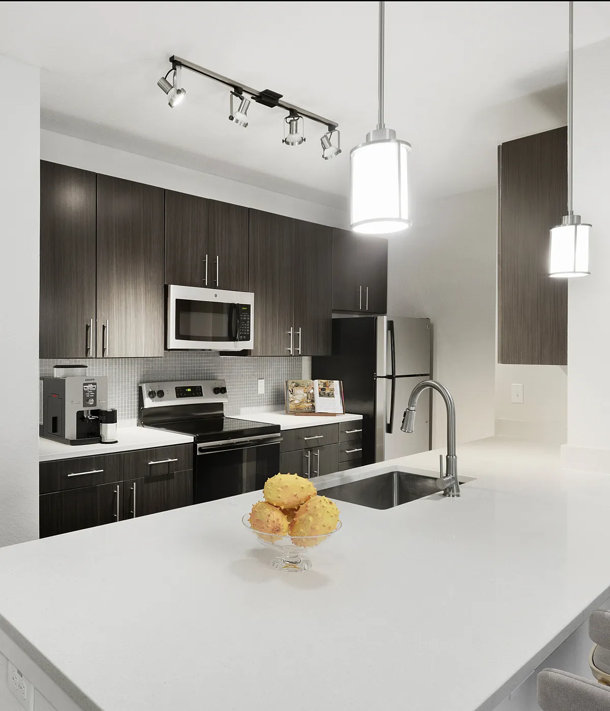 Modern kitchen with sleek dark wood cabinets, stainless steel appliances, and elegant pendant lighting over a spacious white countertop.