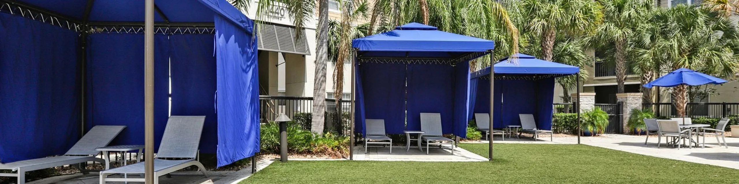 Inviting outdoor lounge area with stylish blue cabanas and lush palm trees for a relaxing retreat.