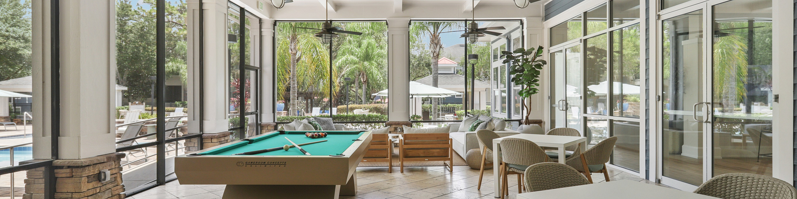 Luxurious recreational area with a pool table, elegant seating, and expansive windows offering a scenic view of a tropical outdoor space.