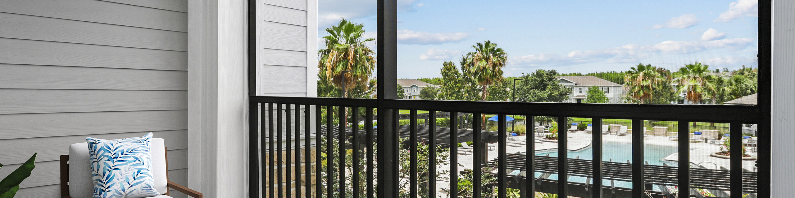 Chic balcony view with elegant outdoor seating overlooking a lush communal pool area and palm trees under a bright blue sky.