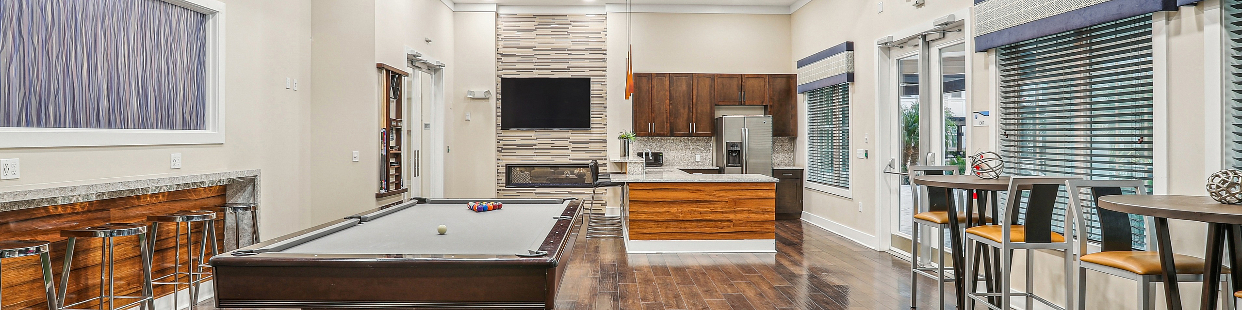 Elegant game and lounge area featuring a sleek billiard table, modern kitchen, and stylish bar seating with hardwood floors and contemporary lighting.