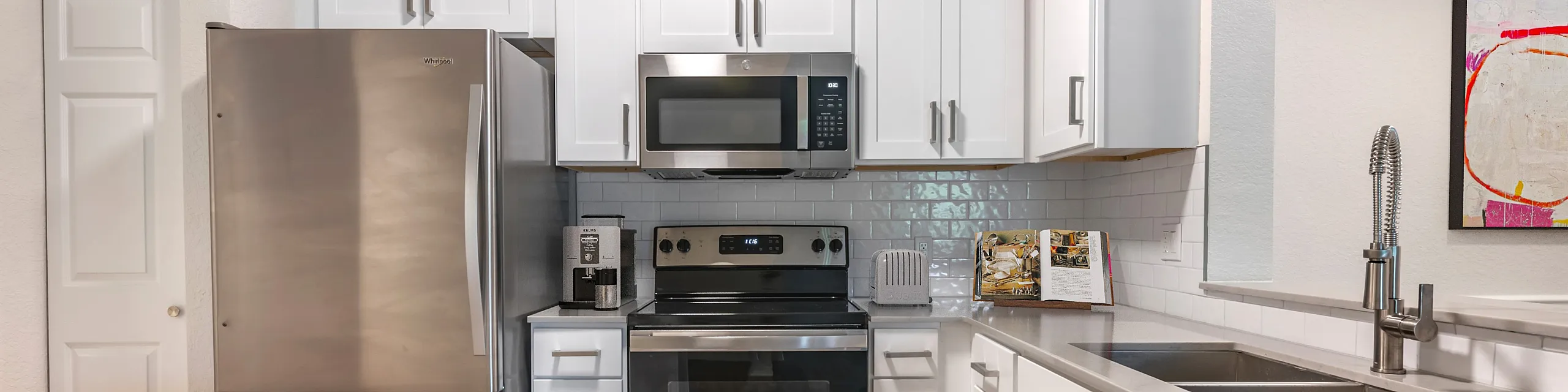 Modern kitchen with stainless steel appliances, white cabinetry, and hardwood floors, featuring a sleek and stylish design.