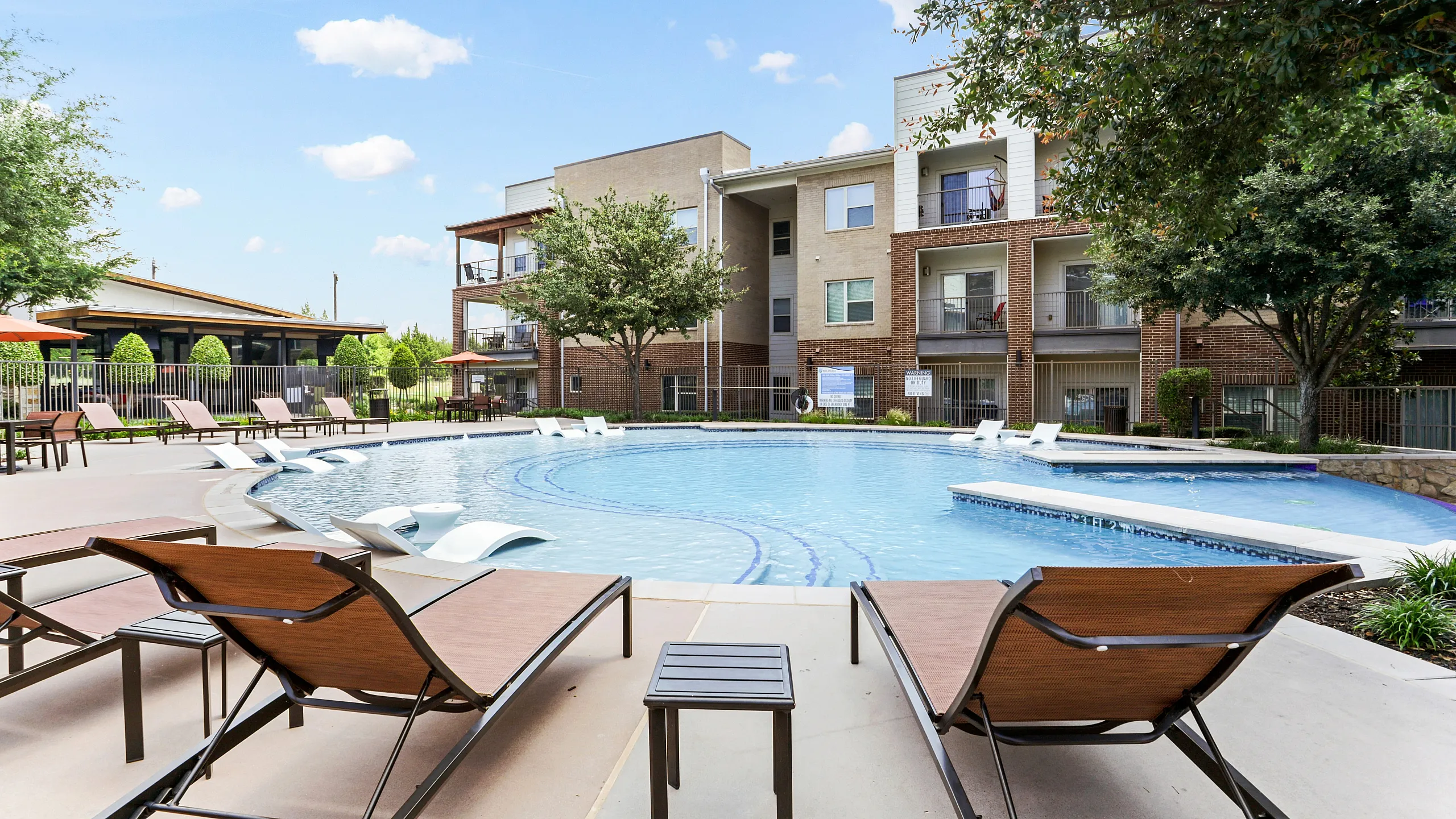 Luxurious apartment community with a serene outdoor pool surrounded by stylish loungers and lush greenery.