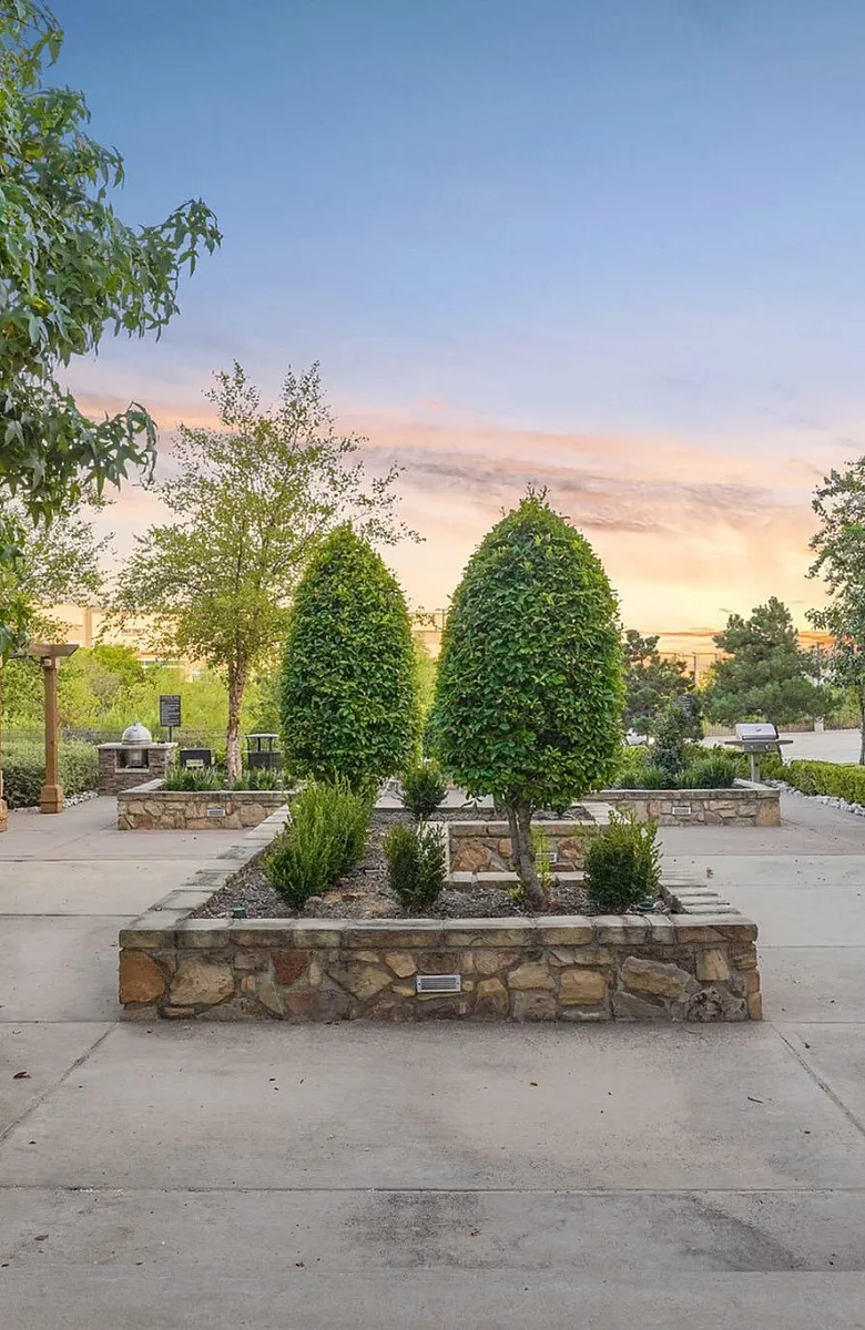 Charming courtyard featuring lush greenery, elegant stone planters, and a cozy pergola under a beautiful sunset sky.