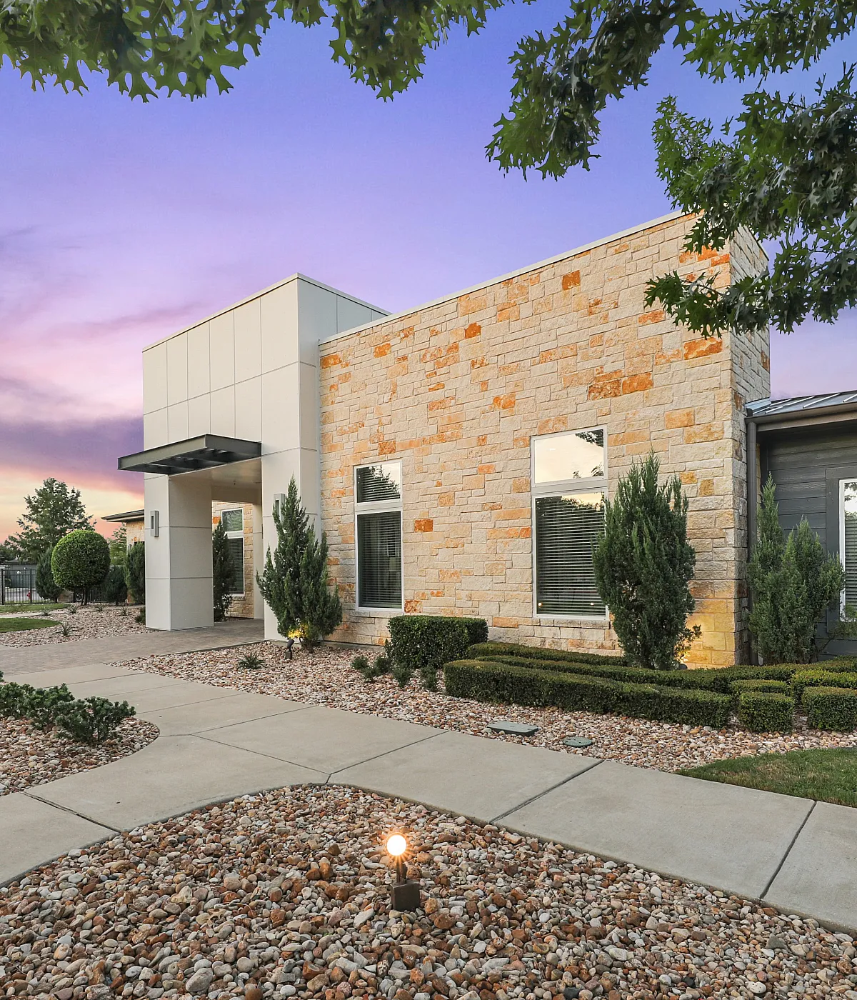 Charming modern apartment exterior with stylish stone facade, manicured landscaping, and a serene walkway under a stunning sunset sky.