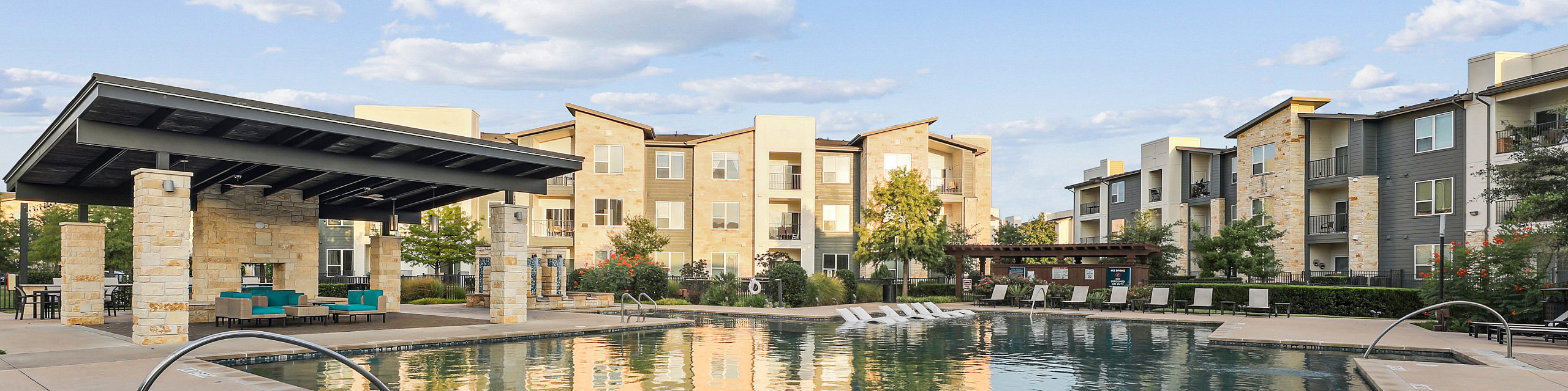 Inviting apartment complex featuring a serene outdoor pool, modern lounge, and lush landscaping under a sunny blue sky.