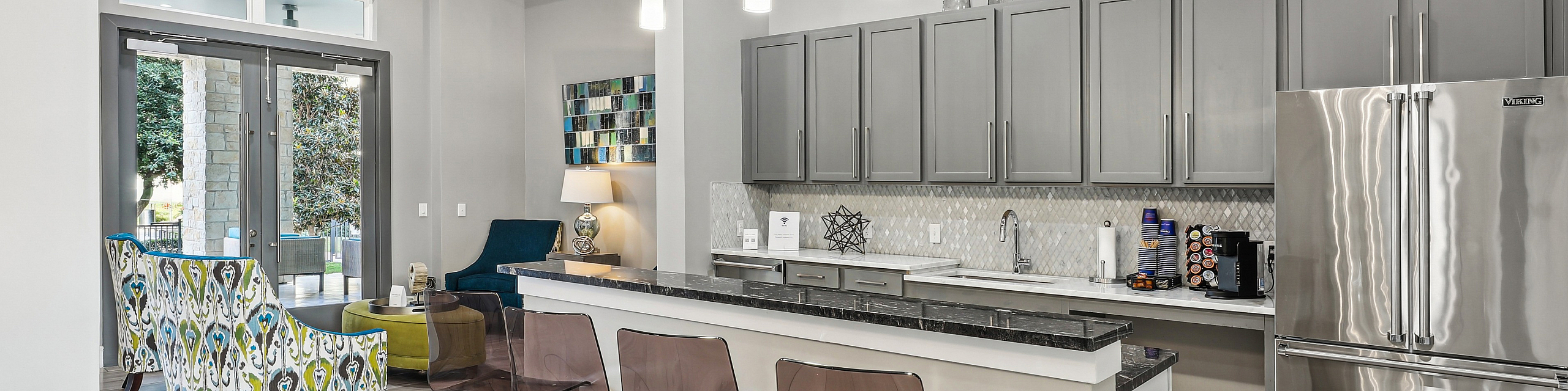 Contemporary kitchen and living area with sleek stainless-steel appliances, elegant gray cabinets, and stylish seating, exuding modern luxury and comfort.