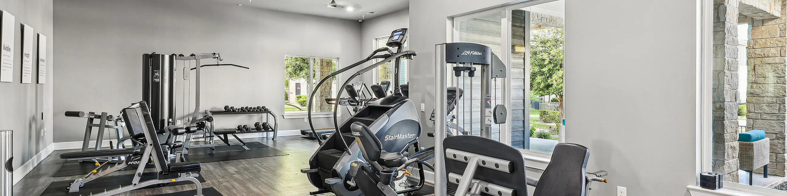 Modern fitness center in an upscale apartment complex featuring state-of-the-art exercise equipment and large windows for natural light.