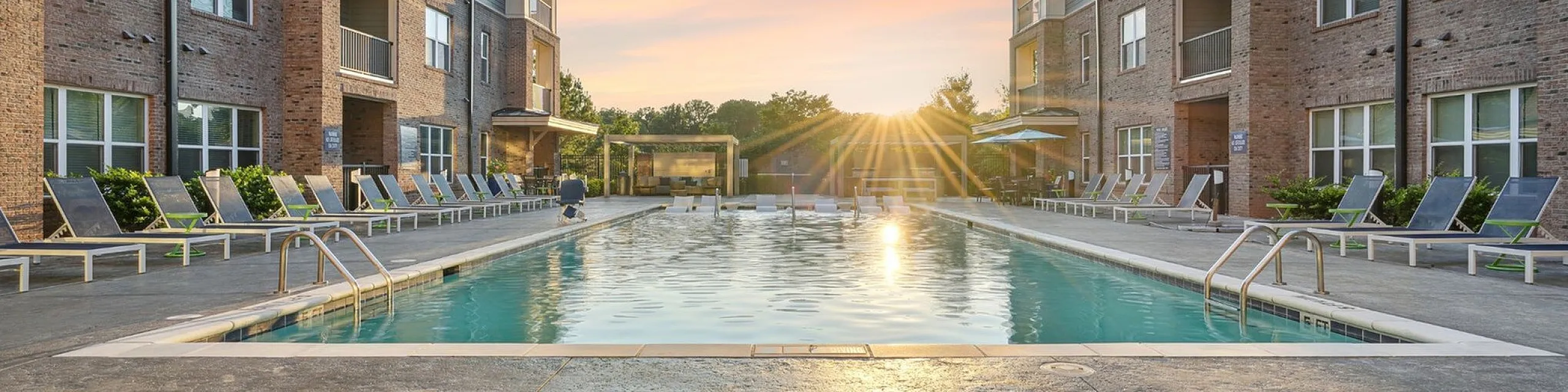 Luxurious apartment complex with a sparkling outdoor pool, sun loungers, and stunning sunset view.