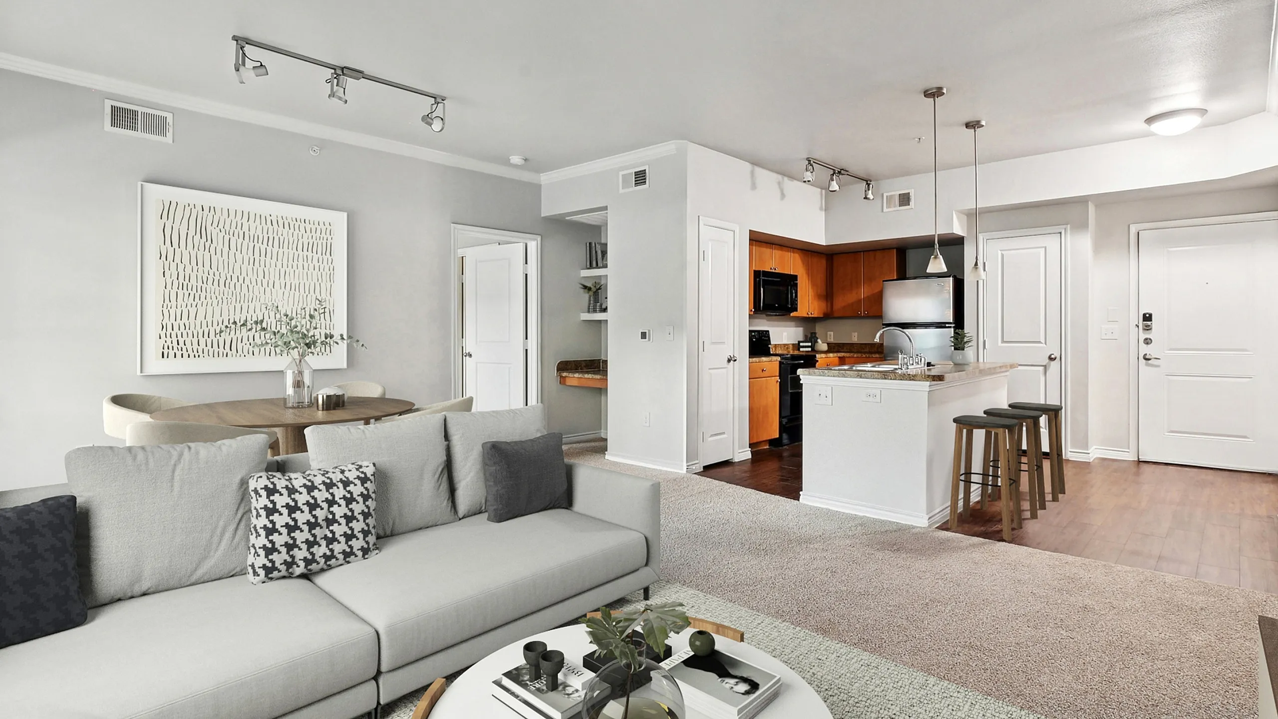Modern open-concept apartment living area featuring a sleek kitchen with granite countertops, cozy dining nook, and stylishly furnished lounge with a plush gray sofa.