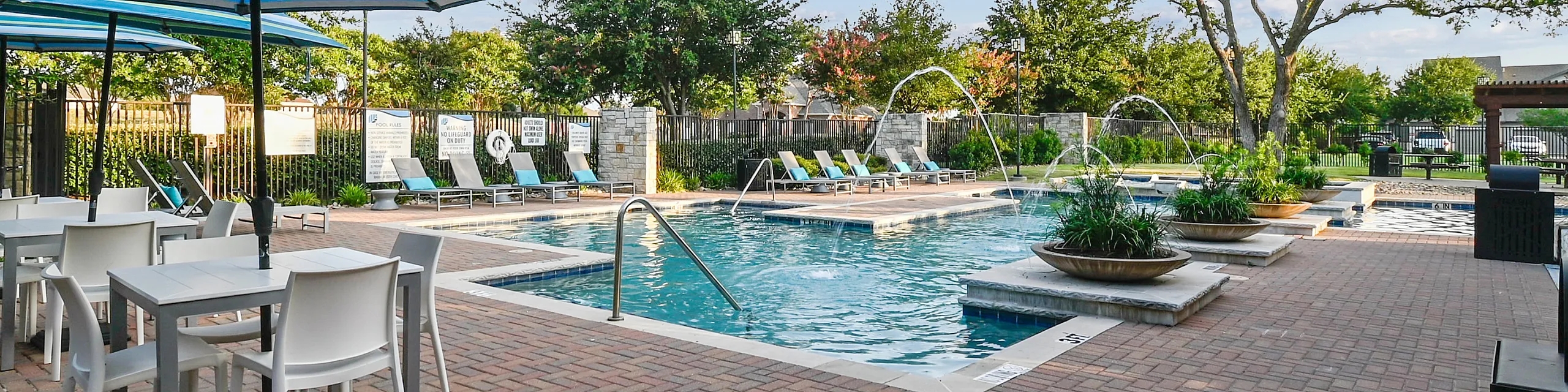 Inviting outdoor pool area with elegant fountain features, surrounded by comfortable lounge chairs and striped umbrellas, perfect for relaxing under a sunny sky.